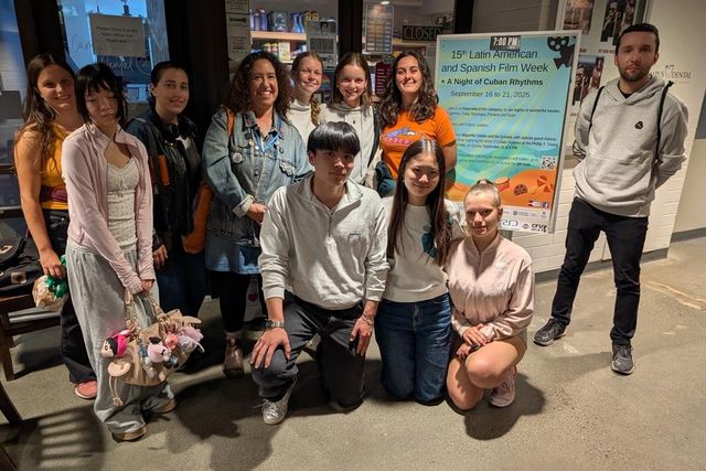 A group of attendees and volunteers posing beside the Film Week poster